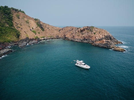 Aerial view of a white yacht anchored in a turquoise bay surrounded by rocky cliffs and sparse vegetation Vasco Da Gama Goa India.