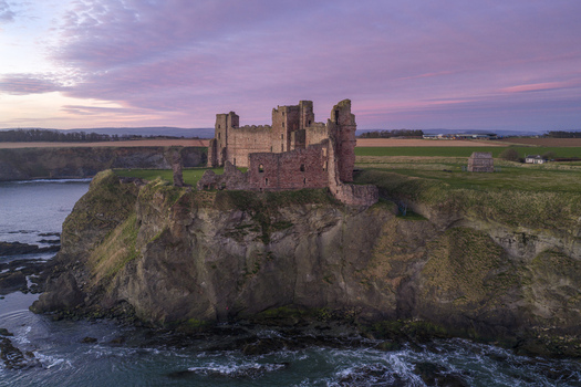 Aerial view of the ruined Tantallon Castle on a cliff edge overlooking the sea during a pink sunset in North Berwick Scotland United Kingdom.