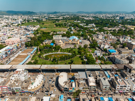 Aerial view of the urban landscape of Udaipur featuring a central park with a pond surrounding buildings and distant hills in Udaipur Rajasthan India.
