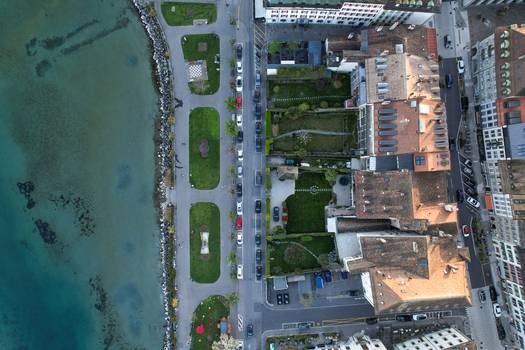 Aerial view of the waterfront promenade with green parks parked cars along the street and historic rooftops by the lake in Morges Vaud Switzerland. Aerial view of the waterfront promenade with green parks parked cars along the street and historic rooftops by the lake in Morges Vaud Switzerland.