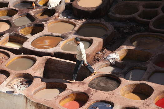 View of a man walking on the narrow stone edges of traditional dye vats at the historic Chouara Tannery in Morocco.