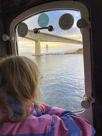 View of a child looking through a window at the Skye Bridge and a lighthouse in the distance on the Isle of Skye United Kingdom. View of a child looking through a window at the Skye Bridge and a lighthouse in the distance on the Isle of Skye United Kingdom.