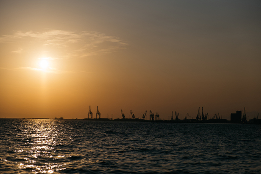 View of the industrial port of Thessaloniki with silhouettes of cargo cranes against the golden sunset sky over the Aegean Sea in Thessaloniki Greece.