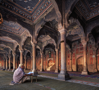 Chiniot Punjab Pakistan 25 January 2013 View of an elderly man reading a book inside the historic Shahi Mosque featuring intricate stone arches and detailed carvings.