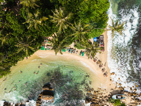 Aerial view of Secret Beach Mirissa with lush palm trees turquoise water people swimming and sunbeds on the sand in Mirissa Southern Province Sri Lanka. Aerial view of Secret Beach Mirissa with lush palm trees turquoise water people swimming and sunbeds on the sand in Mirissa Southern Province Sri Lanka.
