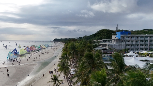 Malay Philippines 02 May 2026 Aerial view of Boracay Island featuring White Beach with tourists colorful sailboats and palm trees under a cloudy sky.