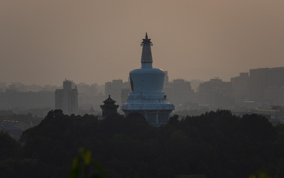 View of the iconic White Dagoba in Beihai Park surrounded by lush trees with the hazy modern skyline of Beijing in the background Beijing Beijing China. View of the iconic White Dagoba in Beihai Park surrounded by lush trees with the hazy modern skyline of Beijing in the background Beijing Beijing China.