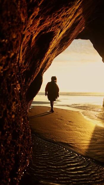 View of a person on a beach framed by a cave New Zealand. View of a person on a beach framed by a cave New Zealand.