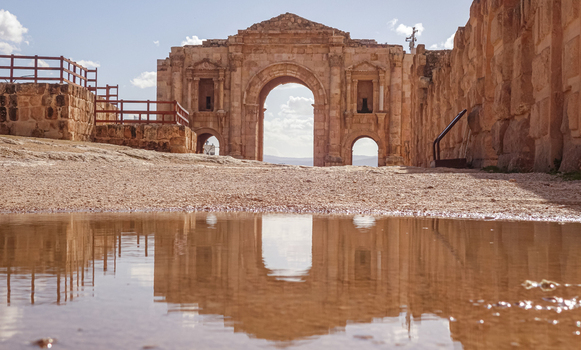 View of the ancient Arch of Hadrian reflected in a puddle on a sunny day in Jerash Jerash Governorate Jordan. View of the ancient Arch of Hadrian reflected in a puddle on a sunny day in Jerash Jerash Governorate Jordan.