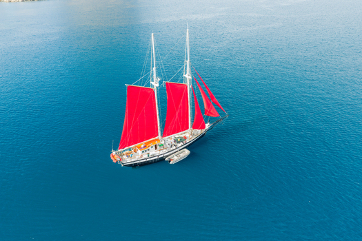 Aerial view of a sailboat with vibrant red sails floating on calm blue water Uummannaq Kitaa Greenland. Aerial view of a sailboat with vibrant red sails floating on calm blue water Uummannaq Kitaa Greenland.