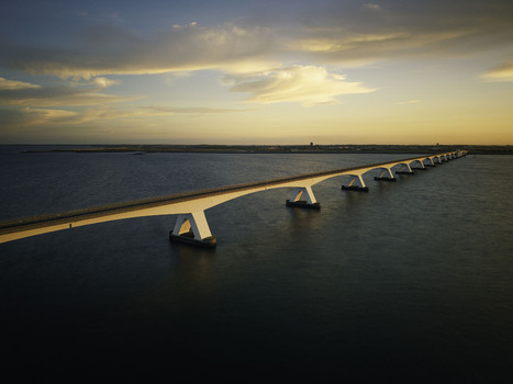 Aerial view of the Zeeland Bridge spanning the Oosterschelde estuary during the golden hour with calm water and a warm sunrise sky in Zierikzee Zeeland Netherlands. Aerial view of the Zeeland Bridge spanning the Oosterschelde estuary during the golden hour with calm water and a warm sunrise sky in Zierikzee Zeeland Netherlands.