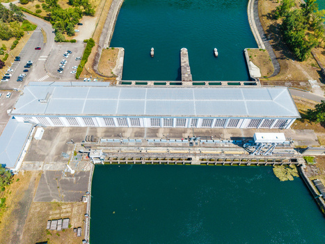 Aerial view of the hydroelectric power plant and lock system on the canal with a long industrial building calm blue water and parking areas in Hombourg Grand Est France.