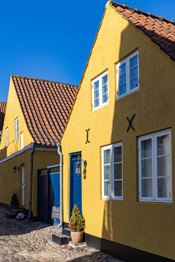 View of historic yellow houses with orange tiled roofs and blue doors along a cobblestone street under a clear blue sky in Ribe Denmark. View of historic yellow houses with orange tiled roofs and blue doors along a cobblestone street under a clear blue sky in Ribe Denmark.