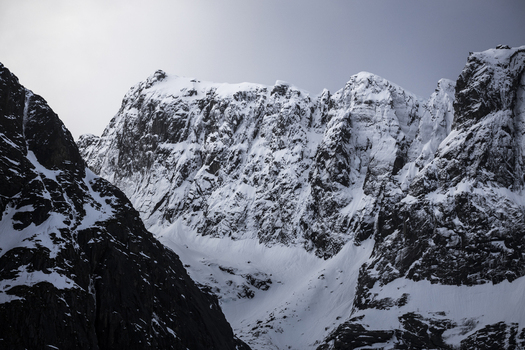 View of snow covered mountain peaks and rugged dark rock faces under an overcast winter sky Kvaloya Troms Norway. View of snow covered mountain peaks and rugged dark rock faces under an overcast winter sky Kvaloya Troms Norway.