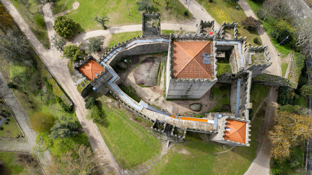 Aerial view of Guimaraes Castle featuring its medieval stone fortifications crenelated towers and surrounding green parkland under soft daylight in Guimaraes Braga Portugal. Aerial view of Guimaraes Castle featuring its medieval stone fortifications crenelated towers and surrounding green parkland under soft daylight in Guimaraes Braga Portugal.