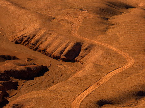 Aerial view of the Atacama Desert with a winding dirt road cutting through the arid rugged reddish brown landscape under dramatic light in Antofagasta Chile.