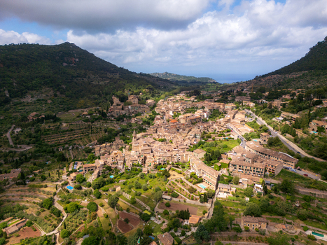 Aerial view of the historic town of Valldemossa with stone houses and terraced gardens nestled in a green valley under a cloudy sky Valldemossa Balearic Islands Spain.