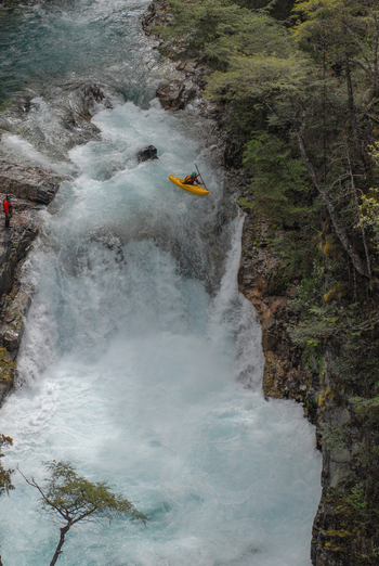 View of a kayaker navigating the white water rapids of the Rio Manso waterfall surrounded by rocky cliffs and lush forest San Carlos de Bariloche Rio Negro Argentina. View of a kayaker navigating the white water rapids of the Rio Manso waterfall surrounded by rocky cliffs and lush forest San Carlos de Bariloche Rio Negro Argentina.