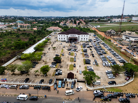 Aerial view of a grand white edifice with a dark roof surrounded by a vast bustling parking lot teeming with dark vehicles and figures Umuahia Abia Nigeria. Aerial view of a grand white edifice with a dark roof surrounded by a vast bustling parking lot teeming with dark vehicles and figures Umuahia Abia Nigeria.