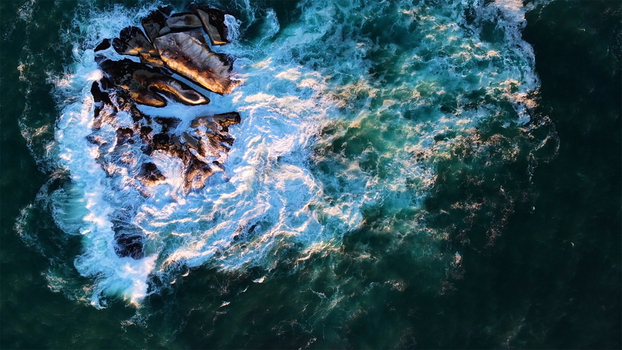 Aerial view of waves crashing against a rocky outcrop with golden sunlight highlights in Cape Town Western Cape South Africa. Aerial view of waves crashing against a rocky outcrop with golden sunlight highlights in Cape Town Western Cape South Africa.