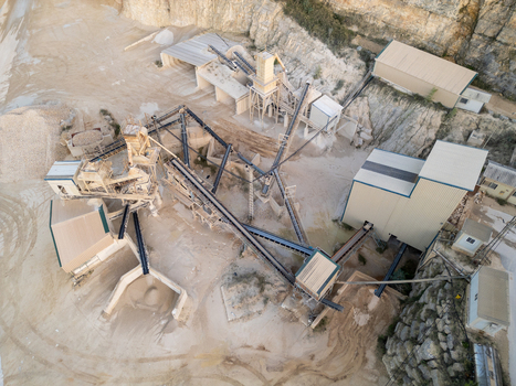 Aerial view of a stone quarry industrial site with conveyor belts processing machinery and storage buildings nestled against a rocky cliff face in Teulada Valencian Community Spain.