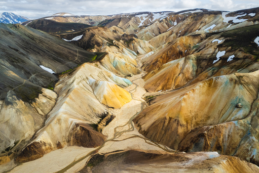 Aerial view of Landmannalaugar rhyolite mountains with vibrant yellow orange and grey slopes a winding riverbed and scattered snow patches in Rangarthing Ytra Iceland. Aerial view of Landmannalaugar rhyolite mountains with vibrant yellow orange and grey slopes a winding riverbed and scattered snow patches in Rangarthing Ytra Iceland.