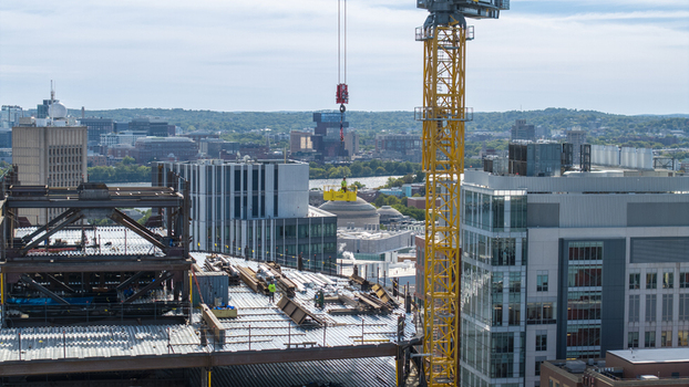 Aerial view of the construction site at Kendall Square featuring a prominent yellow tower crane steel framework and modern urban architecture in Cambridge Massachusetts United States. Aerial view of the construction site at Kendall Square featuring a prominent yellow tower crane steel framework and modern urban architecture in Cambridge Massachusetts United States.