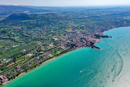 Aerial view of Bardolino on the shores of Lake Garda with turquoise water boats and lush green hills in Provincia di Verona Veneto Italy.