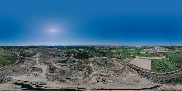 Aerial view of the Yacimiento Arqueologico Cabezo Pequeno del Estano archaeological site surrounded by arid hills and agricultural fields in Alicante Comunidad Valenciana Spain.