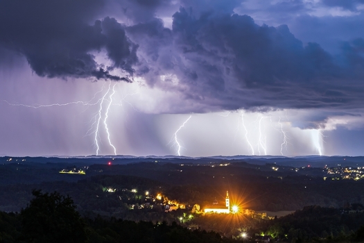 View of intense lightning bolts illuminating a town with the Mariatrost basilica atop the hill under a stormy sky creating a dramatic contrast of light and shadow Graz Styria Austria.