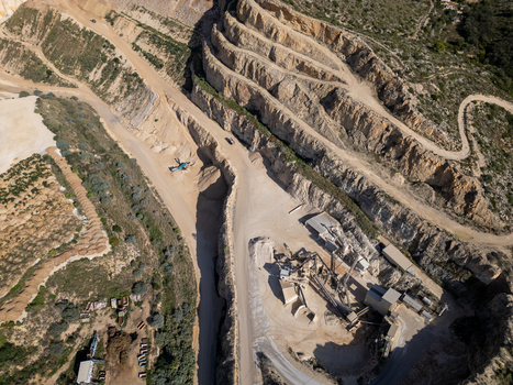 Aerial view of an open pit quarry with terraced rock walls heavy machinery and processing equipment in Teulada Valencian Community Spain.