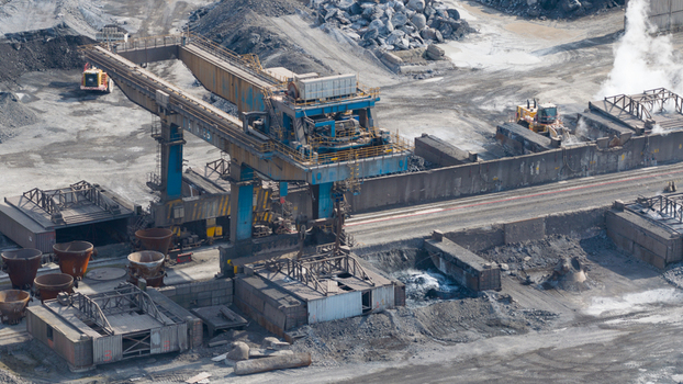Aerial view of Tata Steel industrial plant featuring a massive blue gantry crane and heavy machinery operating amidst piles of raw materials and rising steam in Velsen Noord Noord Holland Netherlands. Aerial view of Tata Steel industrial plant featuring a massive blue gantry crane and heavy machinery operating amidst piles of raw materials and rising steam in Velsen Noord Noord Holland Netherlands.