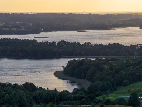 Aerial view of calm lakes surrounded by dense green forests and rolling hills under a soft golden sunset light in Lithuania. Aerial view of calm lakes surrounded by dense green forests and rolling hills under a soft golden sunset light in Lithuania.