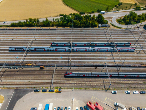 Aerial view of Daniken train station with multiple passenger trains on tracks surrounding agricultural fields and a parking area in Daniken Solothurn Switzerland.