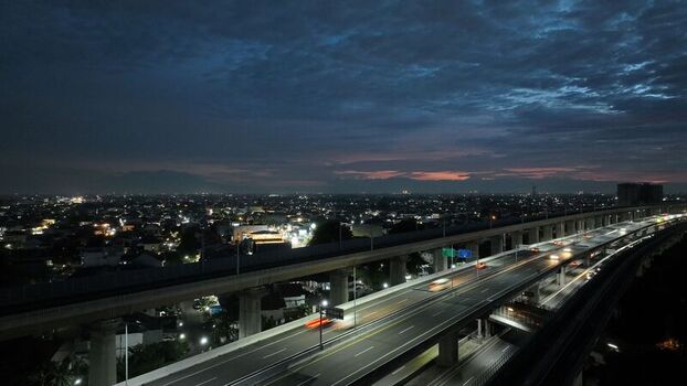 Aerial view of a multi level highway overpass with car light trails at dusk under a dark cloudy sky in Bekasi Barat West Java Indonesia.