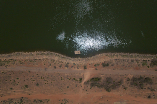 Aerial view of the Minjibir dam with dark green water sun glint a small raft near the shore and an arid landscape with a dirt road in Kano City Kano State Nigeria. Aerial view of the Minjibir dam with dark green water sun glint a small raft near the shore and an arid landscape with a dirt road in Kano City Kano State Nigeria.