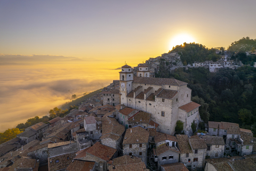 Aerial view of the historic town of Artena with its prominent church and clock tower surrounded by stone houses with terracotta roofs at sunset above a sea of clouds in Artena Lazio Italy.
