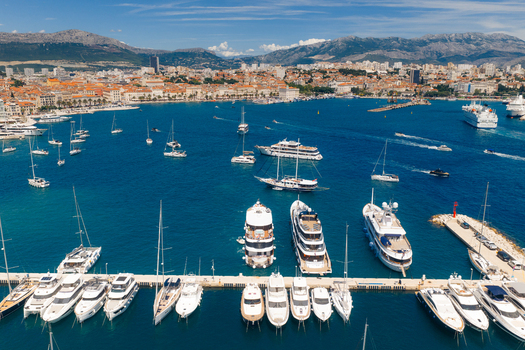 Aerial view of luxury yachts and sailboats moored in the harbor with the historic city and mountains under a clear blue sky in Split Split Dalmatia County Croatia. Aerial view of luxury yachts and sailboats moored in the harbor with the historic city and mountains under a clear blue sky in Split Split Dalmatia County Croatia.