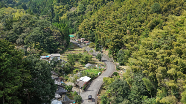 Aerial view of a winding road through a lush forested mountainous area with small houses and bamboo groves in Shimizu Ward Shizuoka Shizuoka Japan. Aerial view of a winding road through a lush forested mountainous area with small houses and bamboo groves in Shimizu Ward Shizuoka Shizuoka Japan.