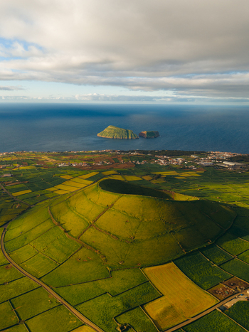 Aerial view of Pico Dona Joana geodesico volcanic crater surrounded by green agricultural fields and stone walls overlooking the Atlantic Ocean in Feteira Acores Portugal. Aerial view of Pico Dona Joana geodesico volcanic crater surrounded by green agricultural fields and stone walls overlooking the Atlantic Ocean in Feteira Acores Portugal.