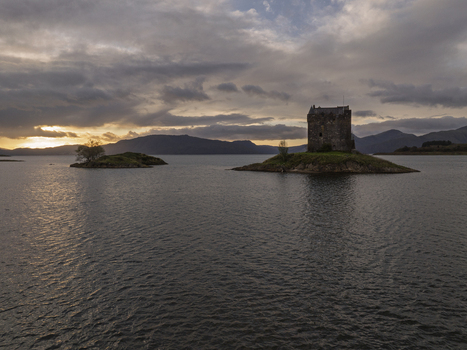 Aerial view of Castle Stalker situated on a small island in a loch surrounded by mountains under a dramatic sunset sky in Scotland United Kingdom. Aerial view of Castle Stalker situated on a small island in a loch surrounded by mountains under a dramatic sunset sky in Scotland United Kingdom.