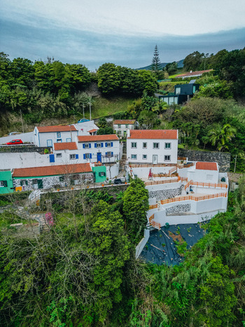Aerial view of quaint white buildings with terracotta roofs nestled into the verdant hillside framed by lush green trees and a distant tower Agua de Alto Azores Portugal.