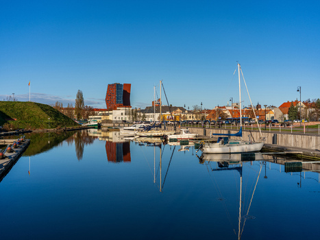 View of sailboats docked along the Dane River with the modern K Tower building reflecting in the calm water under a clear blue sky in Klaipeda Klaipeda County Lithuania. View of sailboats docked along the Dane River with the modern K Tower building reflecting in the calm water under a clear blue sky in Klaipeda Klaipeda County Lithuania.