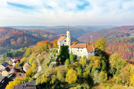 Aerial view of Gossweinstein Castle perched on a rocky hill surrounded by vibrant autumn foliage and the village rooftops in Gossweinstein Bayern Germany.