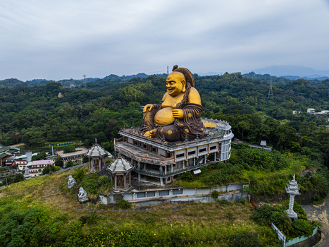 Aerial view of the large golden Maitreya Buddha statue perched on a lush green hillside with surrounding temple structures in Jiuru Township Pingtung County Taiwan. Aerial view of the large golden Maitreya Buddha statue perched on a lush green hillside with surrounding temple structures in Jiuru Township Pingtung County Taiwan.