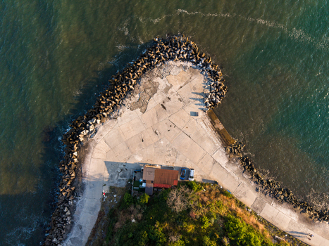 Aerial view of a concrete pier extending into the sea featuring a small building parked cars and protective rock armor along the coastline in Kiten Burgas Bulgaria. Aerial view of a concrete pier extending into the sea featuring a small building parked cars and protective rock armor along the coastline in Kiten Burgas Bulgaria.