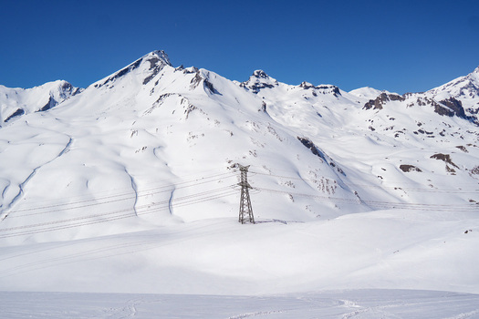 Aerial view of Colle del Piccolo San Bernardo with snow covered mountain peaks and a high voltage electricity pylon under a clear blue sky in La Thuile Valle d Aosta Italy. Aerial view of Colle del Piccolo San Bernardo with snow covered mountain peaks and a high voltage electricity pylon under a clear blue sky in La Thuile Valle d Aosta Italy.