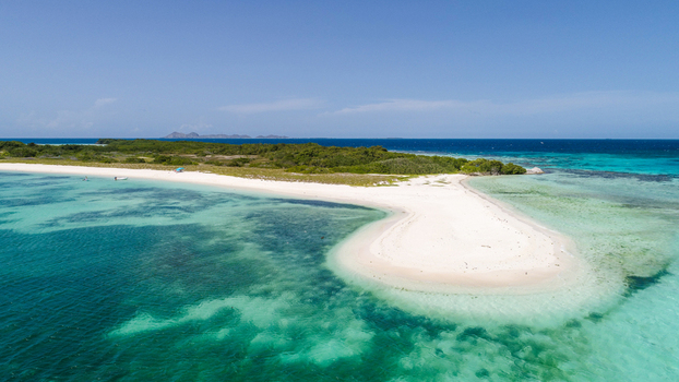 Aerial view of Los Roques archipelago featuring a white sandbar surrounded by turquoise waters and lush vegetation under a clear blue sky in Los Roques Dependencias Federales Venezuela. Aerial view of Los Roques archipelago featuring a white sandbar surrounded by turquoise waters and lush vegetation under a clear blue sky in Los Roques Dependencias Federales Venezuela.