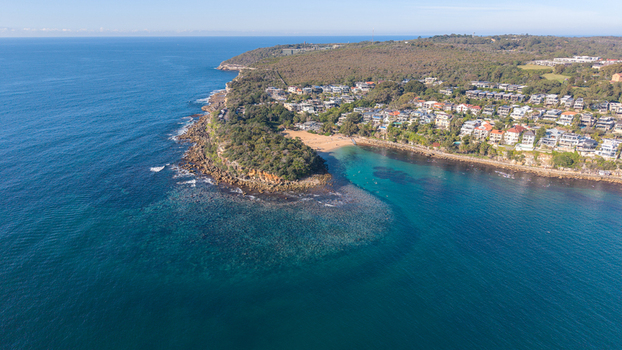 Aerial view of Cabbage Tree Bay Aquatic Reserve featuring turquoise water rocky cliffs and residential houses on the coast in Manly New South Wales Australia.