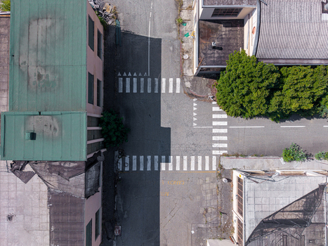 Aerial view of a street intersection with marked crosswalks adjacent buildings with green and grey roofs and shadows cast across the asphalt Casale Monferrato Piedmont Italy. Aerial view of a street intersection with marked crosswalks adjacent buildings with green and grey roofs and shadows cast across the asphalt Casale Monferrato Piedmont Italy.
